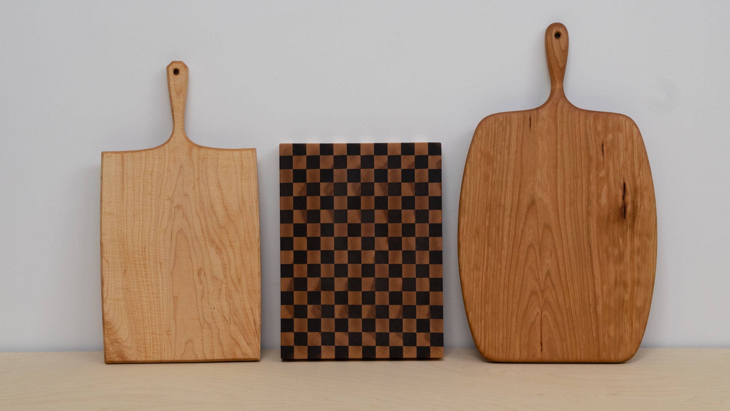 Three wooden cutting boards with different designs on a plain background