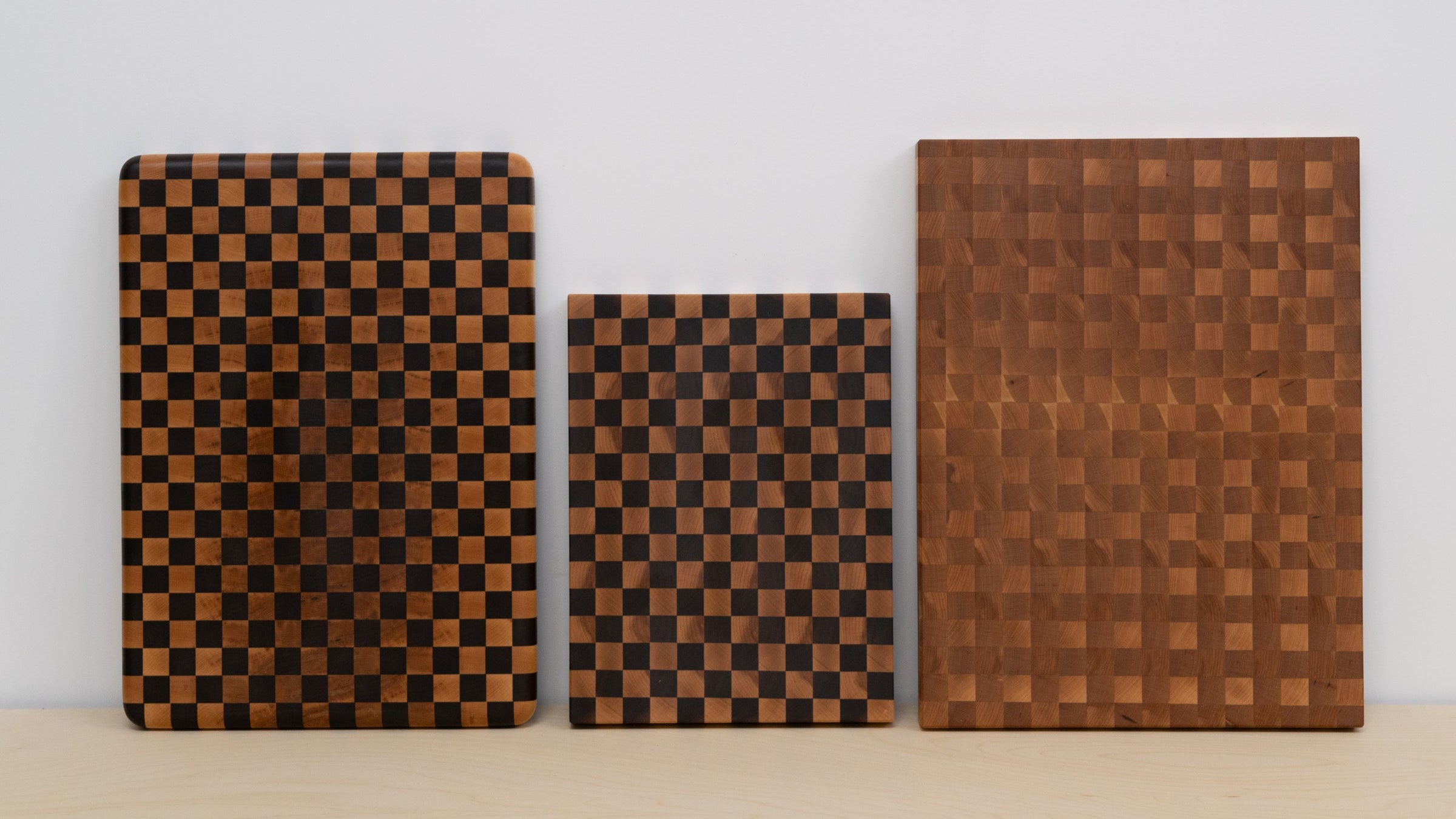 Three wooden cutting boards with checkered and solid patterns on a light background