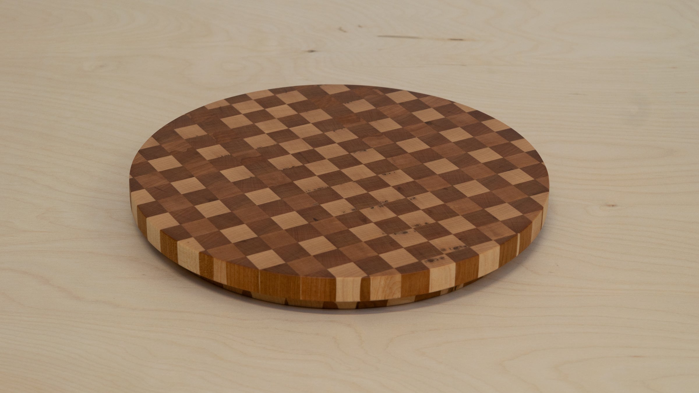 Round wooden cutting board with a checkered pattern on a light wood surface