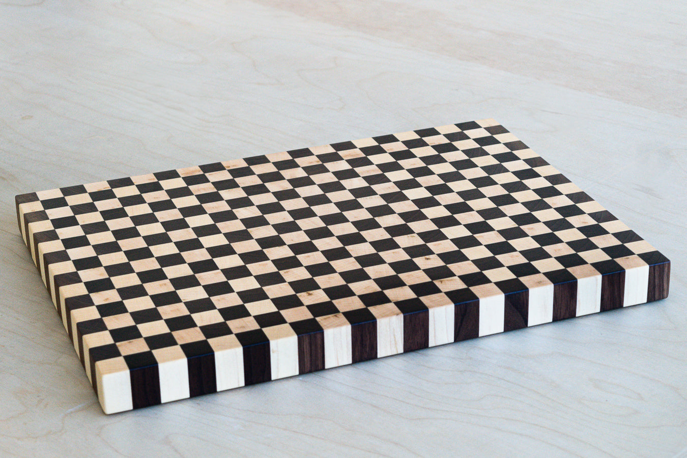Large wooden cutting board, in a checkboard pattern, on a light wood background. 