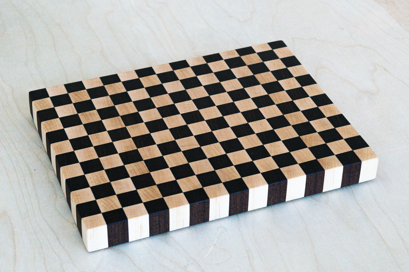 Checkered cutting board with black and beige squares on a light wooden surface